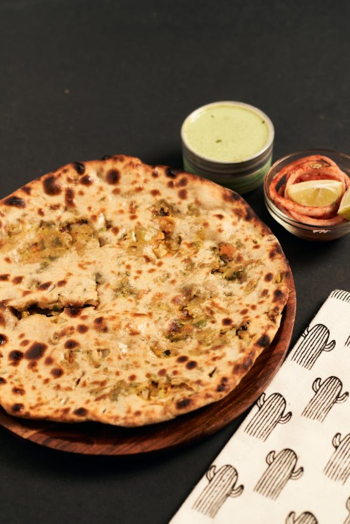 A close-up of homemade stuffed paratha served with green chutney and lime on a wooden plate.